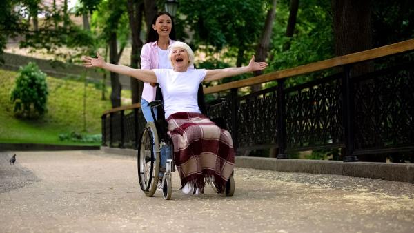 Anziana su sedia a rotella che parla con una volontaria in giardno